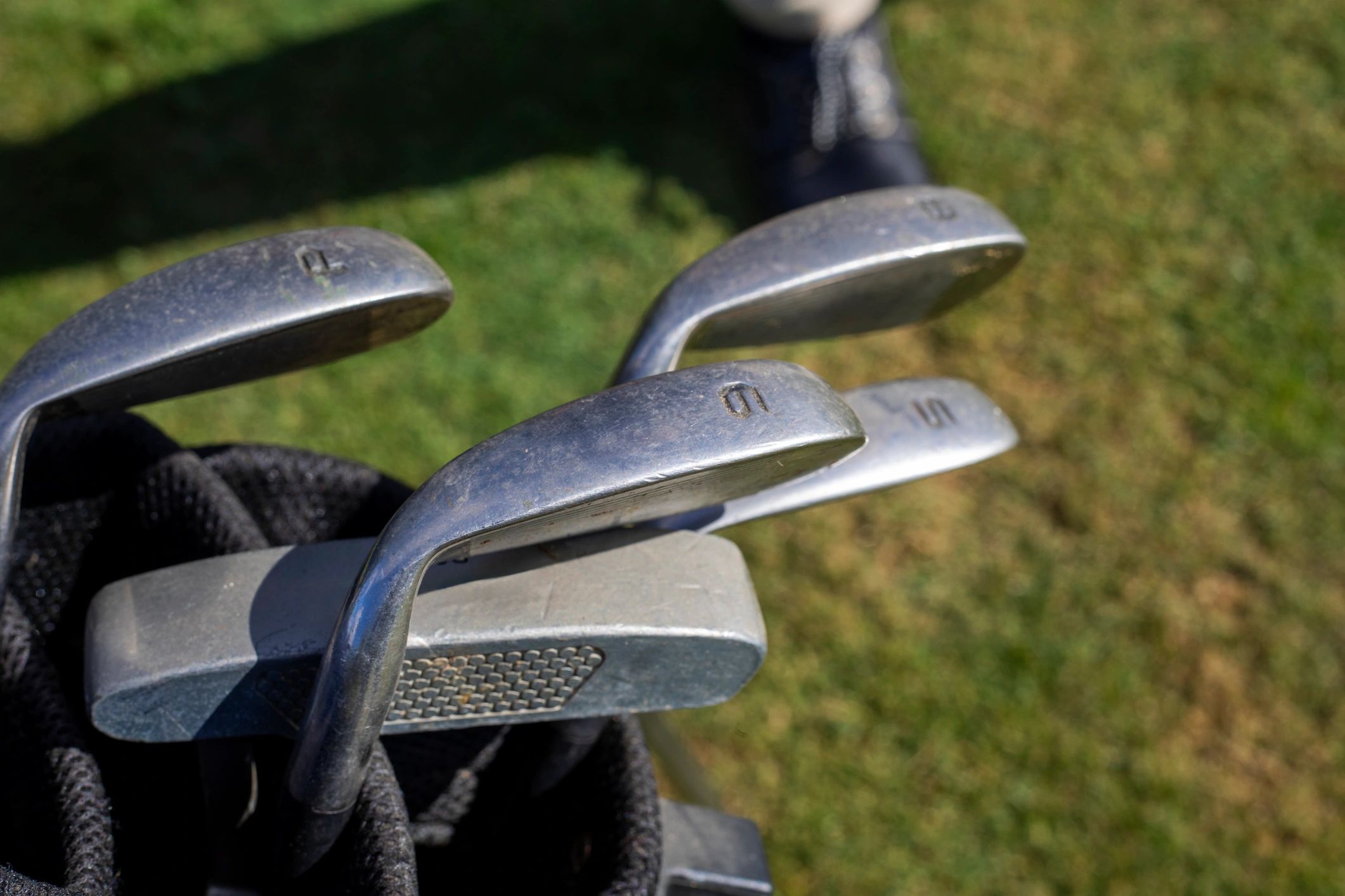 Close-up of golf clubs in a bag on a sunny course